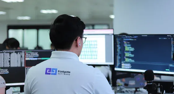 An engineer in an Eastgate polo shirt working at a desk with code displayed across multiple monitors.