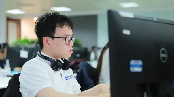Engineer with headphones focused on code at a monitor in an open office