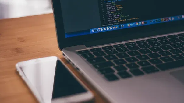 Laptop showing front-end code on a desk beside a smartphone